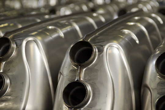 Industrial background. Stacks of new exhausts and silencers mufflers car before distribution and retail. Detail of a new automotive components in stainless steel. Close up.

