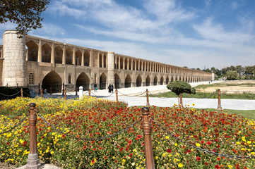 Iran, Isfahan, Pol-e Khaju: Blick auf die Khajoo-Brücke mit Blumen im Vordergrund. Die Brücke hat 23 Bögen, ist 133 Meter lang und 12 Meter breit.
