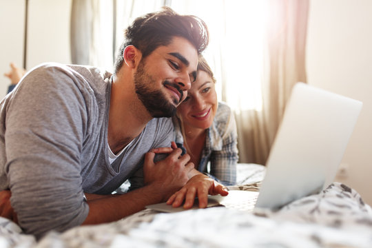Young married couple lying on bed at home and using laptop.