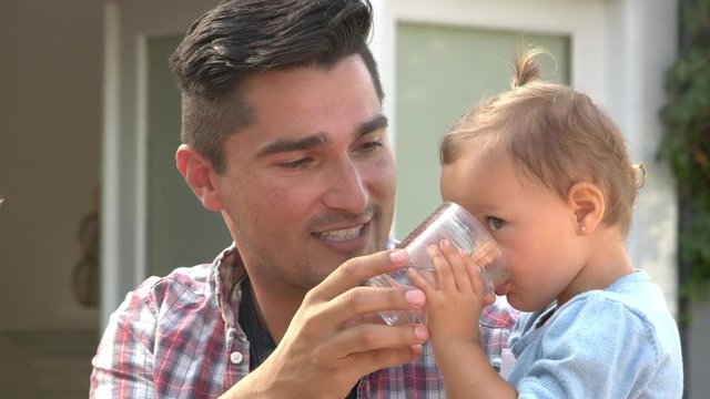 Father Helping Young Daughter To Drink At Outdoor Meal