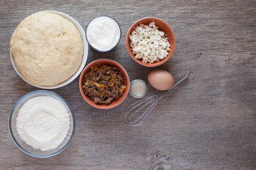 Turkish pasties pogaca ingredients on the grey wooden table: ready dough, flour, yogurt, feta cheese with herbs and mince; yeast and whisk; selective focus on the dough
