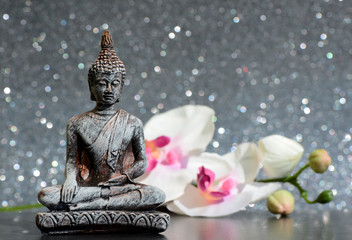 Buddha statue and a orchid flower on a bright shiny glitter background with bokeh