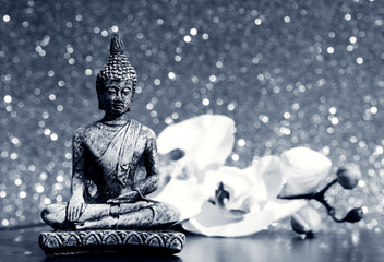Buddha statue and a orchid flower on a bright shiny background with bokeh. Photo in vintage style
