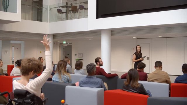 Teacher presenting to a university class, some raising hands