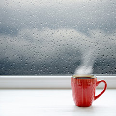 Cup of coffee on a windowsill. In the background window with raindrops and clouds