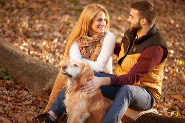 Romantic couple with dog sitting on a tree, autumn forest backgr