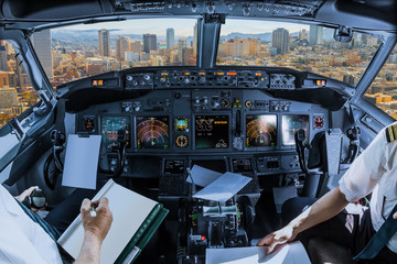 Airplane cockpit flying on San Francisco Financial District Downtown, California, United States, with pilots arms and blank white papers for copy space. © bennymarty