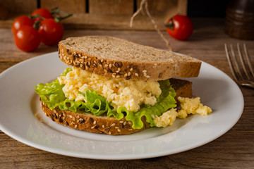 Breakfast sandwich with scrambled eggs, fresh green salad and whole wheat bread. Close up view, horizontal