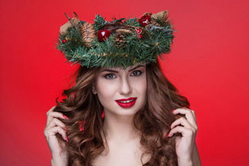 Christmas or New Year beauty girl portrait isolated on red background. Beautiful woman with luxury makeup and christmas wreath on head. Christmas mood.