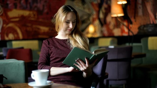 Blonde girl answers cellphone while reading book in the cafe
