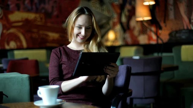 Girl drinking coffee while browsing internet on tablet in the cafe

