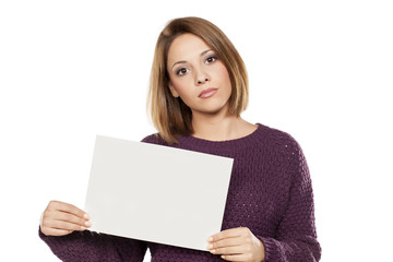 serious young beautiful woman holding a blank sheet of paper for advertising