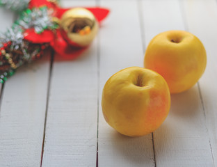two yellow apples and Christmas decoration on white wood background.