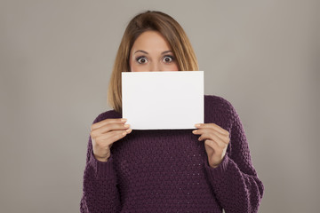 happy young woman peeking behind a blank sheet of paper for advertising