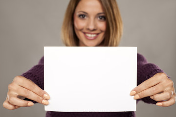 Naklejka premium happy young woman holding a blank sheet of paper for advertising