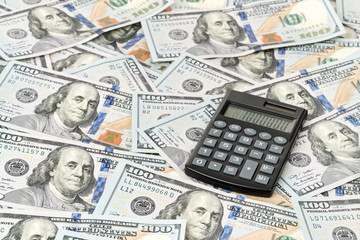 Little black calculator with solar batteries lying on hundred dollar bill