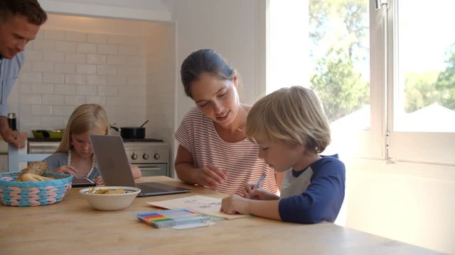 Kids working at kitchen table with mum, while dad cooks