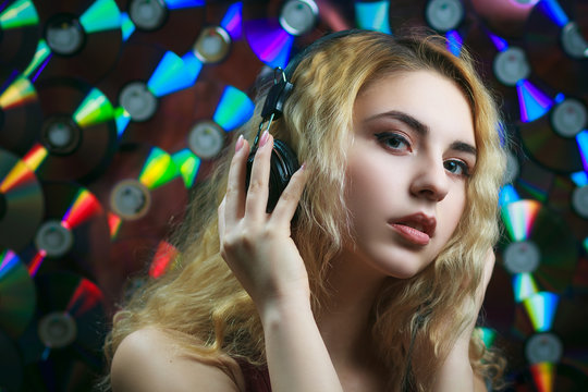 Concept: hipster lifestyle, relaxation. Beautiful young woman in headphones have fun and listen music with colorful CD's on background.