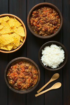 Chili con carne with rice and tortilla chips, photographed on dark wood with natural light