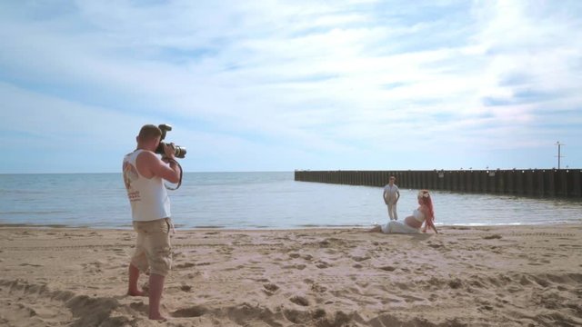 Photographer take photo of love couple on beach. Photo shooting of pregnant couple beach. Man taking picture of pregnant woman lying on sea beach. Photographer taking photo of pregnant couple
