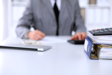 Fototapeta premium Binders with papers are waiting to be processed with business woman back in blur. Accounting planning budget, audit and insurance concept