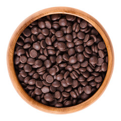 Dark chocolate drops in wooden bowl, ingredient used for cookies and muffins. Edible brown cocoa product. Isolated macro food photo close up from above on white background.
