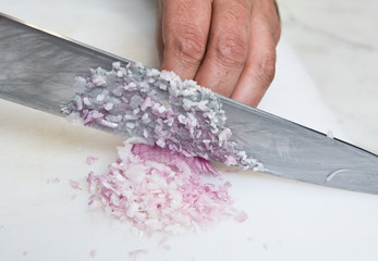 A knife dicing fresh organic Shallots, on a white cutting board.
