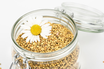 Vitamin jar for immune system, protection, energy. Get well soon. Greeting. Closeup of bee pollen granules in glass jar. Health,healthy jar. Daisy flower. Isolated,white background, copy space.