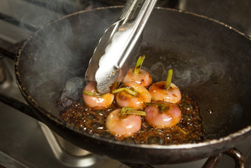 Fresh organic baby turnips, in a metal frying pan, being cooked and caramelised in a sauce.
