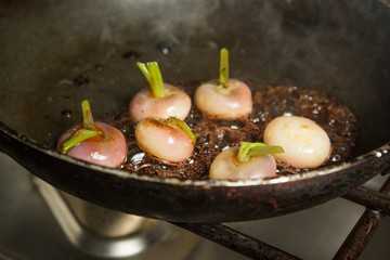 Fresh organic baby turnips, in a metal frying pan, being cooked and caramelised in a sauce.