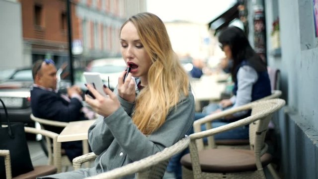 Girl using smartphone as a mirror while painting her lips
