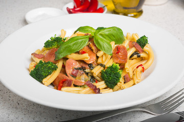 A delicious fresh gourmet Italian strozzapreti pasta dish, with pancetta, italian sausage, broccoli, vegetables, topped with fresh basil.