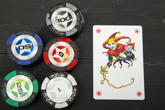 Joker and chips to play poker on a black wooden table