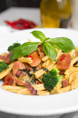 A delicious fresh gourmet Italian strozzapreti pasta dish, with pancetta, italian sausage, broccoli, vegetables, topped with fresh basil.