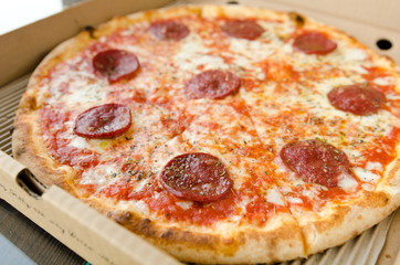 Juicy pepperoni pizza with melted mozzarella cheese and oregano sprinkle, served in a takeaway box