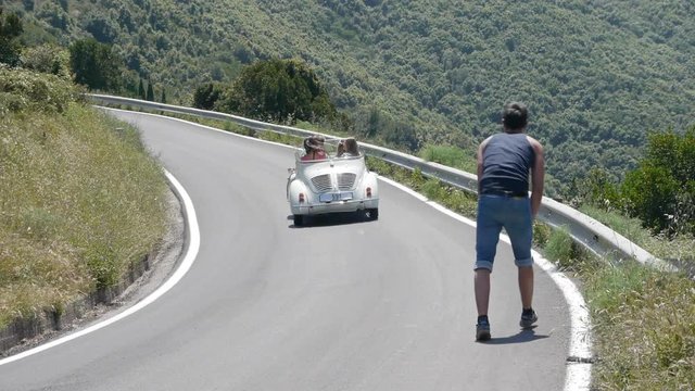 Four friends in convertible driving past hitchhiker
