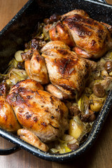 Beautiful golden , crispy oven roasted, free range whole chickens, on a bed of roasted vegetables in a metal baking tray.