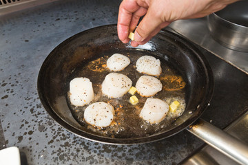 Delicious pan seared organic scallops being seared in melted butter, in a metal cooking pan on the hob. Presented professionally and shot with a shallow depth of field.