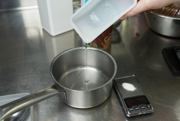 A container of clear sugar syrup being poured into a metal pan, ready for cooking.