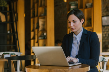 Beautiful young woman is seating indoors at a cafe restaurant and looking at laptop