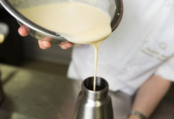 Thick fresh sweet dessert cream, being poured into a metal container in an industrial kitchen.
