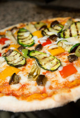 Close up of a Vegetarian thin crust  pizza, with grilled courgette, peppers, aubergine, artichoke, cheese and tomato topping