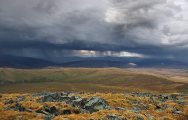 Rain from the storm dramatic dark scary clouds and a highland bright steppe with rocks and stones in the foreground Plateau Ukok Altai mountains, Siberia, Russia