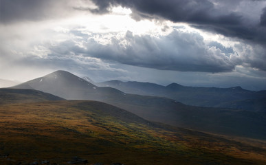 Dark mountain under a stormy evening dramatic cloudy sky with dark clouds and bright rays of sunset light Plateau Ukok Altai mountains Siberia, Russia