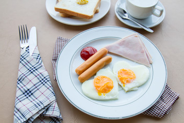 Breakfast with fried egg, ham, sausage, toast, butter, and coffee on table.