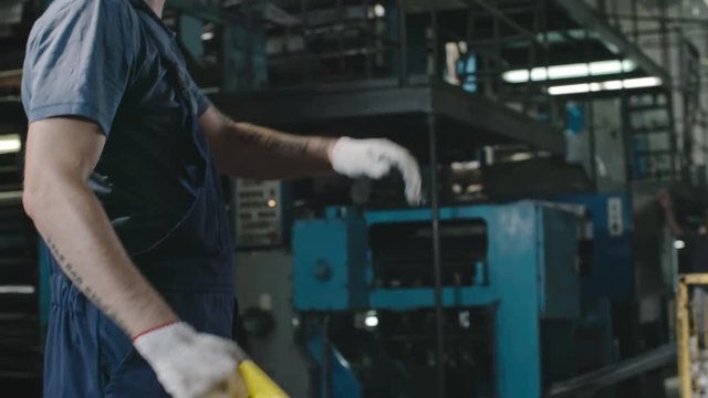 PAN of tired factory worker taking off hard hat and wiping his forehead with hand, then looking at camera