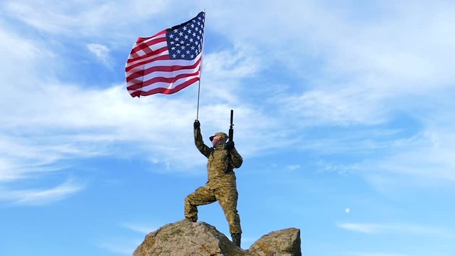 Soldier on mountain top with automatic rifle,  and  American Flag. Slow Motion. 