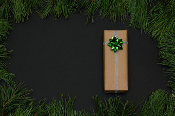 Frame of pine branches. Gift wrapped in kraft paper, decorated with ribbon silver and bow green....