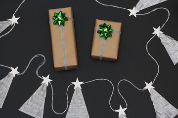 Christmas gifts wrapped in kraft paper. Two  bow green and silver colors. Garland from herringbone. Black background, top view, flat lay