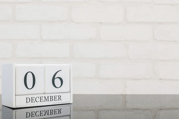 Closeup white wooden calendar with black 6 december word on black glass table and white brick wall textured background with copy space , selective focus at the calendar